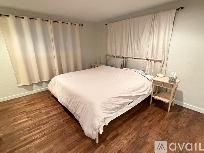 A bedroom with a bed, nightstand, and window with curtains.