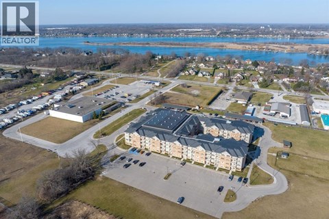 A realtor logo is on the top left corner of an aerial view of a residential area with a swimming pool and a large building.