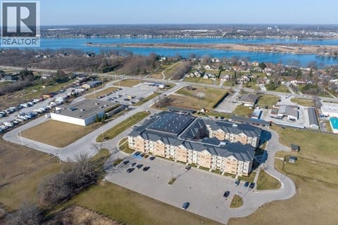 A realtor logo is on the top left corner of an aerial view of a residential area with a swimming pool and a large building.