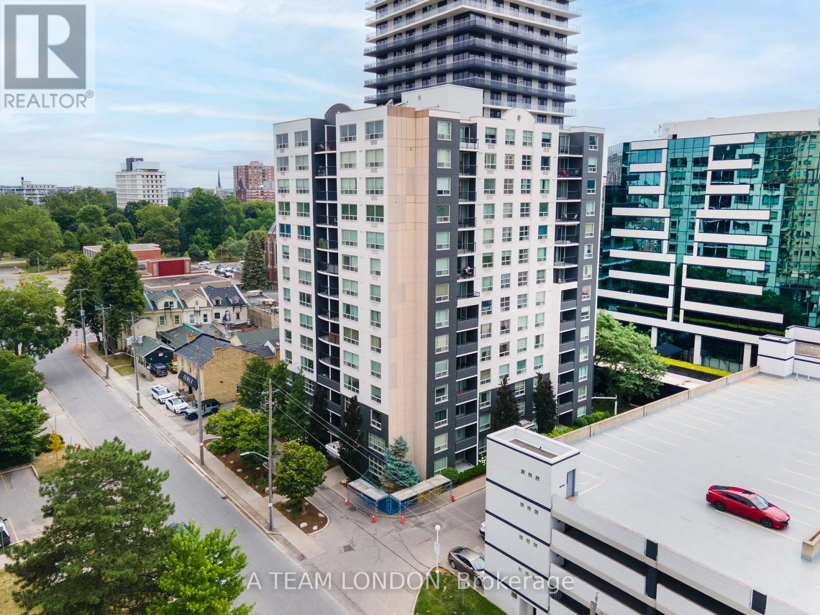 A tall building with a balcony is in the middle of a street with cars and trees.
