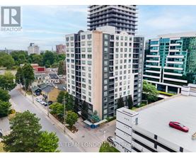 A tall building with a balcony is in the middle of a street with cars and trees.