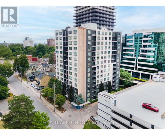 A tall building with a balcony is in the middle of a street with cars and trees.