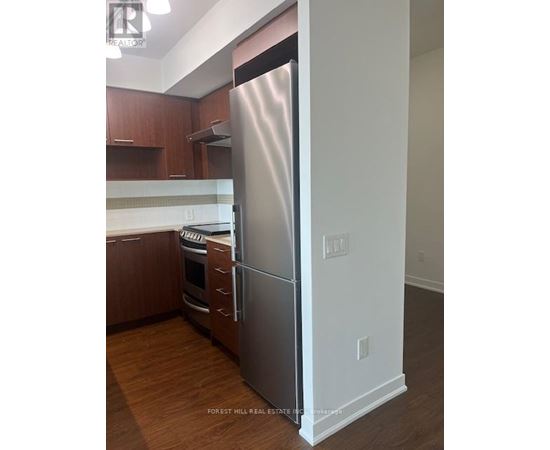 A stainless steel refrigerator stands in a kitchen with wooden cabinets.