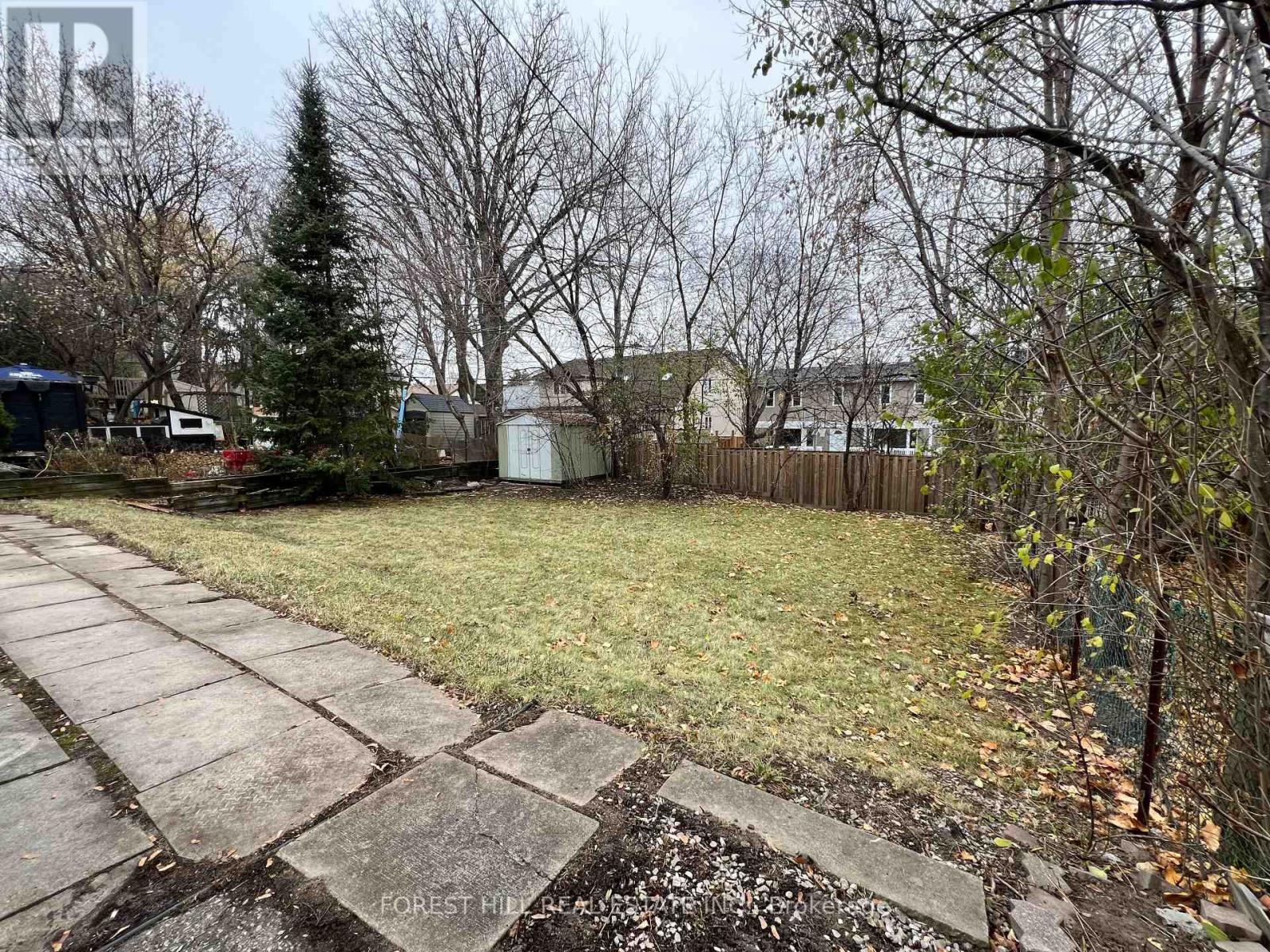 A backyard with a concrete walkway and a small tree.