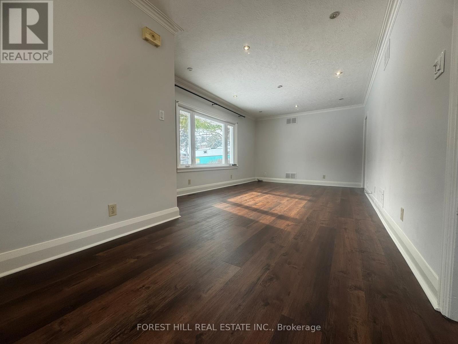 A room with wooden floors and white walls, with a window letting in natural light.