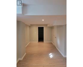 A spacious room with wooden flooring and white walls, with a black door at the end of the hallway.