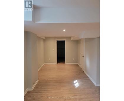 A spacious room with wooden flooring and white walls, with a black door at the end of the hallway.