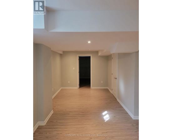 A spacious room with wooden flooring and white walls, with a black door at the end of the hallway.