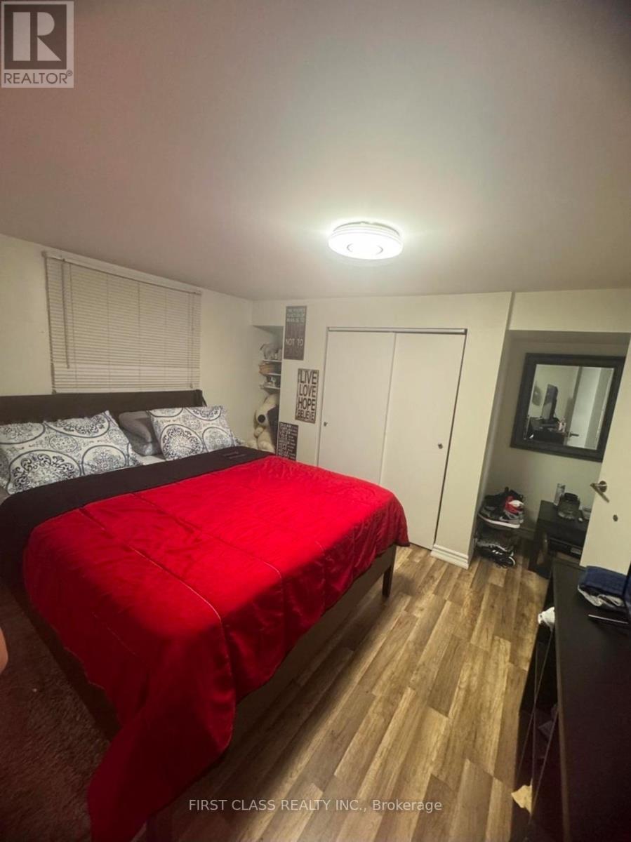 A bedroom with a red bedspread and a wooden floor.