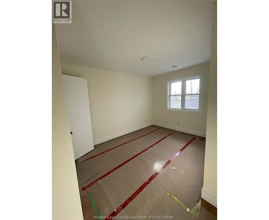 A room with a white door and a window with red tape on the floor.