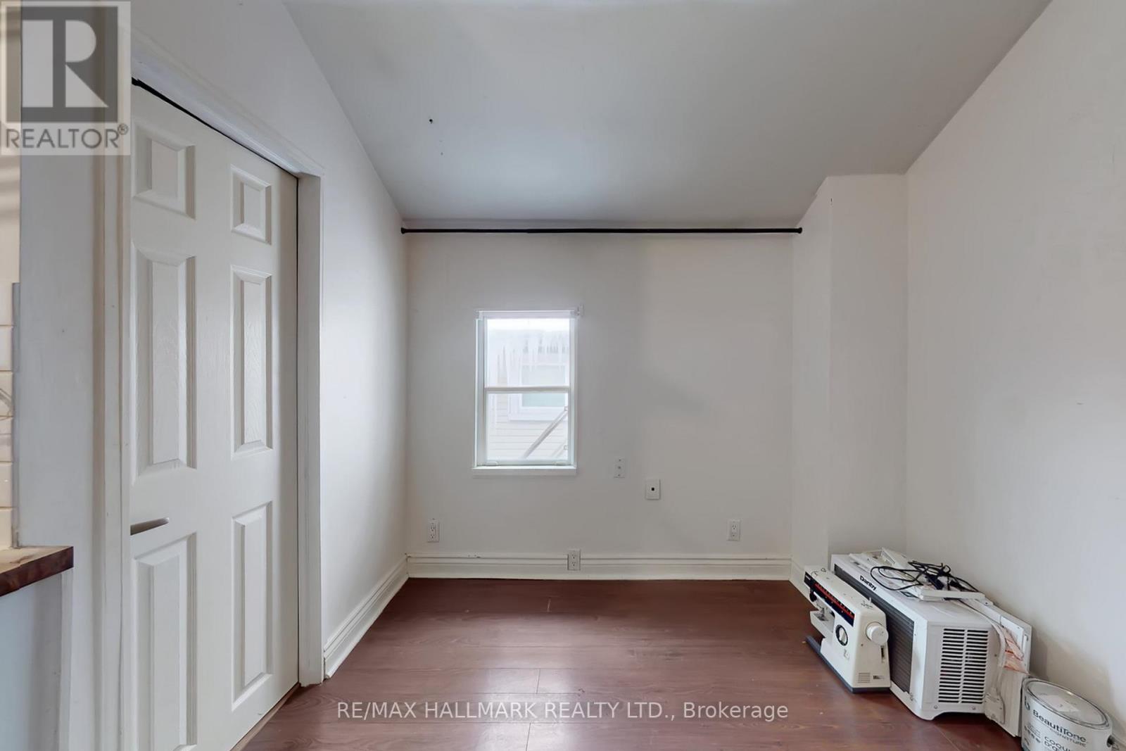 A room with a white door, a window, and a wooden floor.