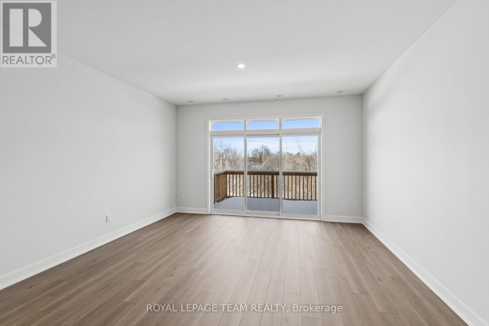 A spacious room with wooden flooring and a large window overlooking a wooden fence.