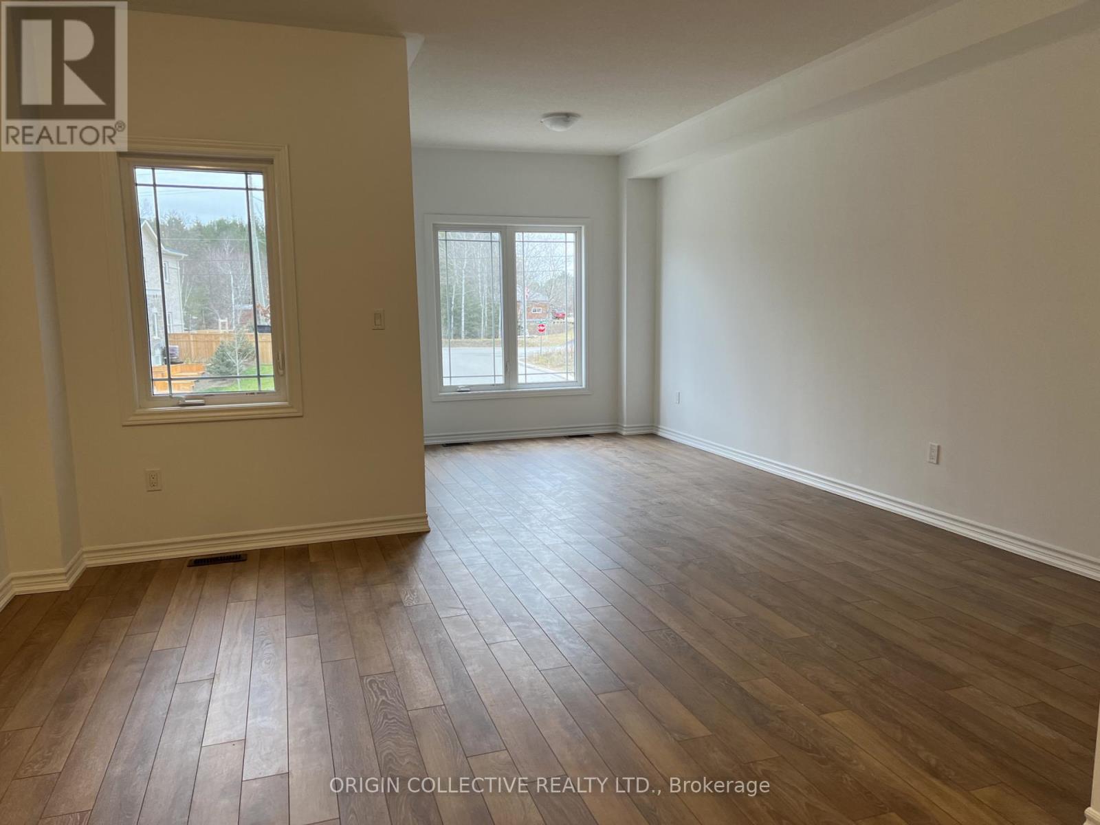 A spacious room with wooden flooring and two windows.