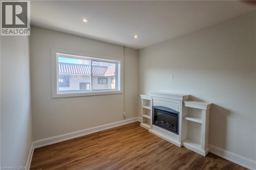A white fireplace in a room with wooden floors and a window.