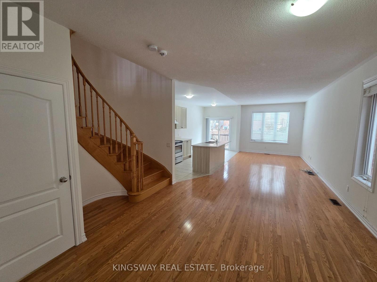 A spacious room with wooden flooring and a staircase leading to another level.