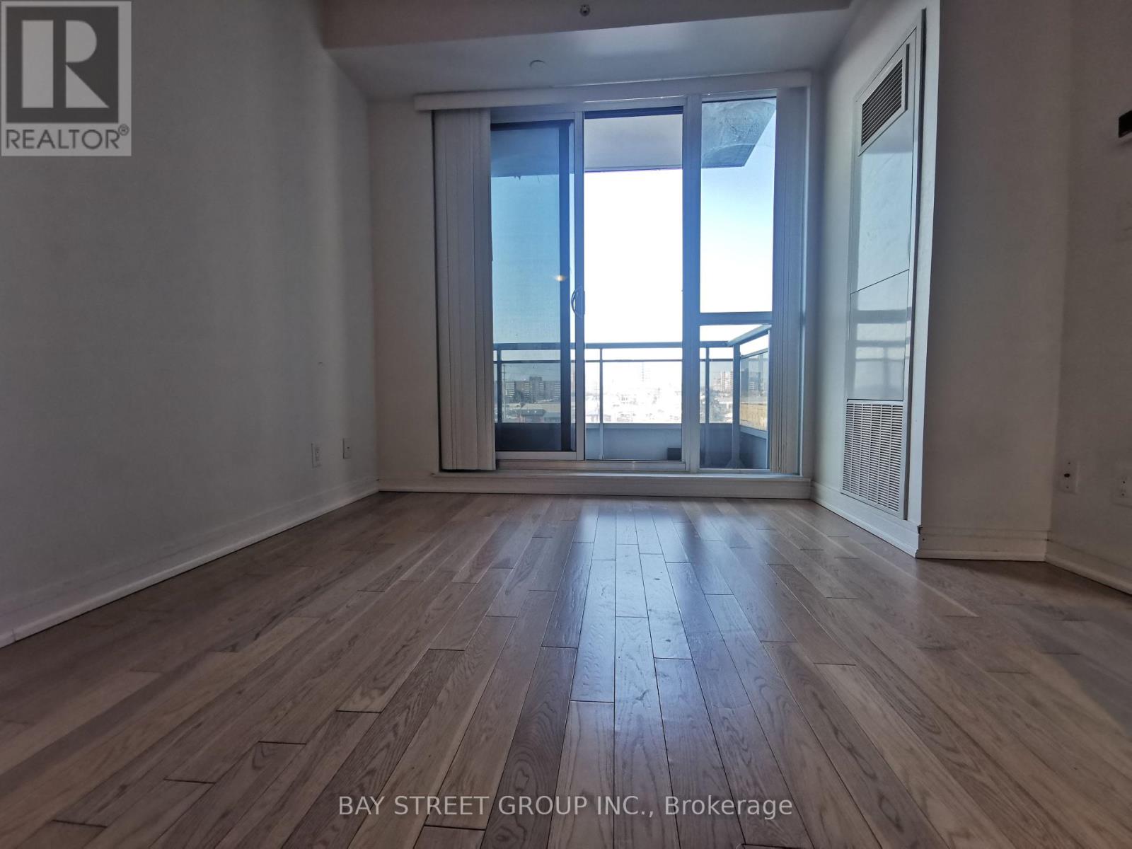 A spacious room with wooden flooring and a large window overlooking a balcony.