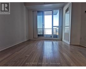 A spacious room with wooden flooring and a large window overlooking a balcony.