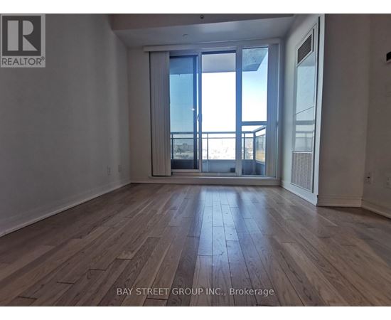 A spacious room with wooden flooring and a large window overlooking a balcony.
