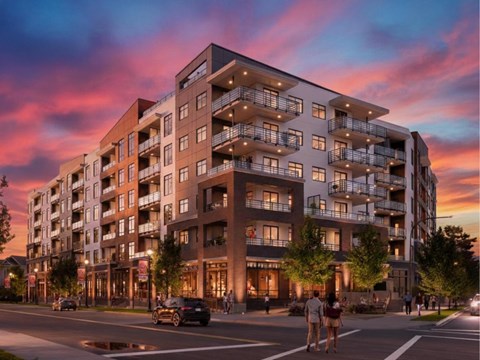A modern apartment building with balconies and multiple stories is shown with people walking on the sidewalk.