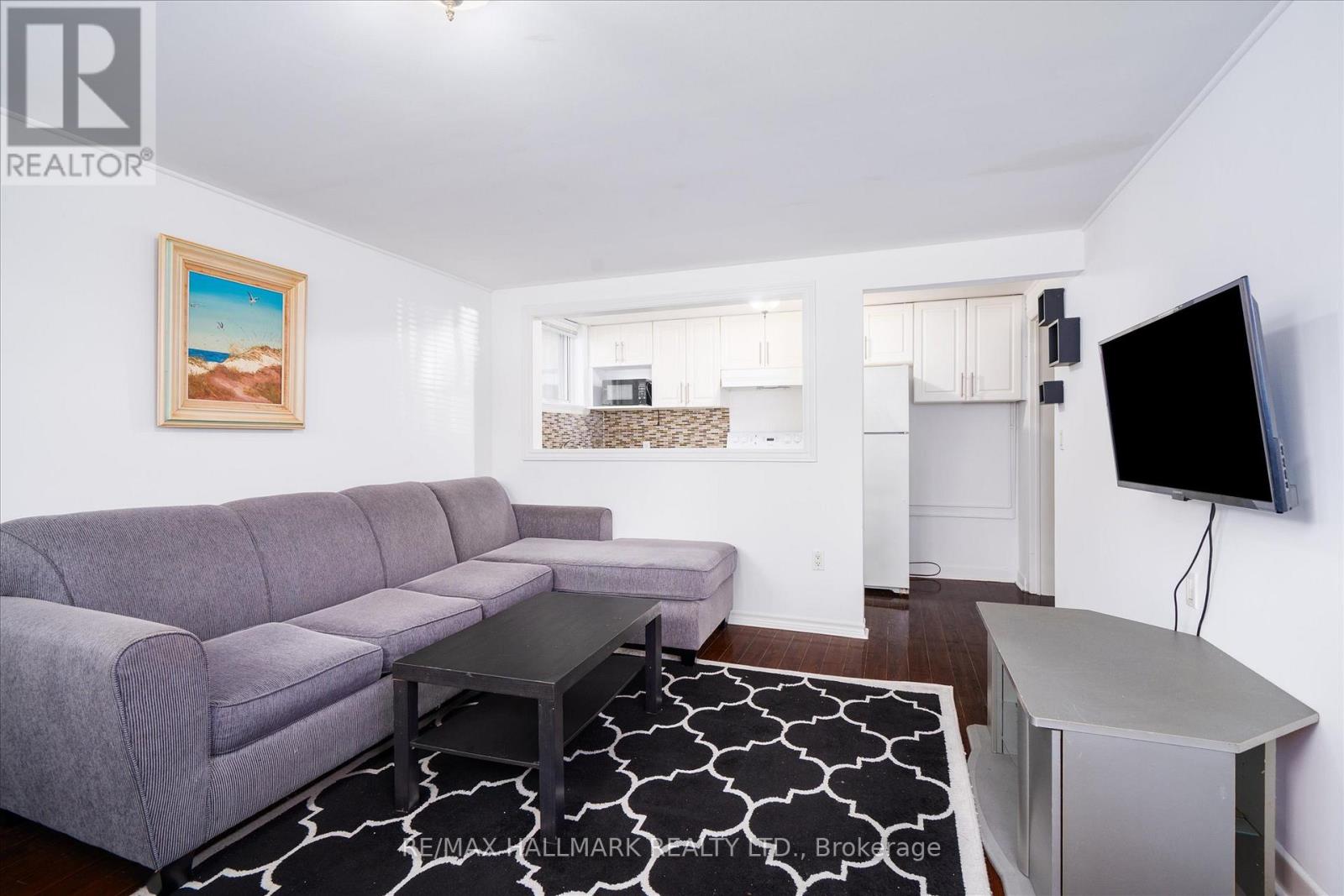 A living room with a grey couch and a painting of a beach scene on the wall.