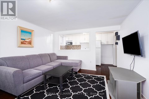 A living room with a grey couch and a painting of a beach scene on the wall.