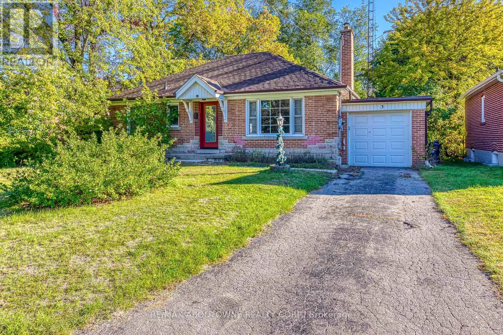 A house with a red door and a garage is surrounded by greenery.