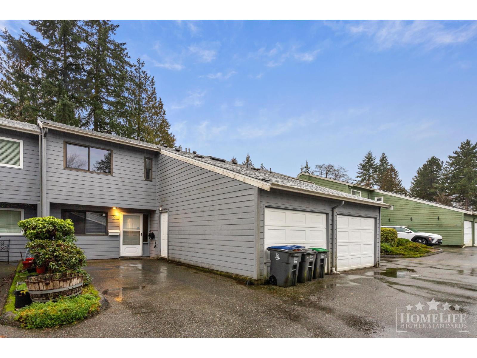 A grey house with a garage and a driveway with a bush.