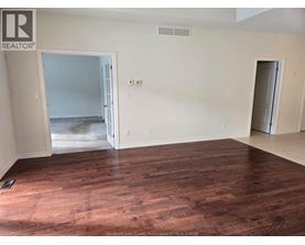 A room with wooden floors and white walls, with a doorway leading to another room.