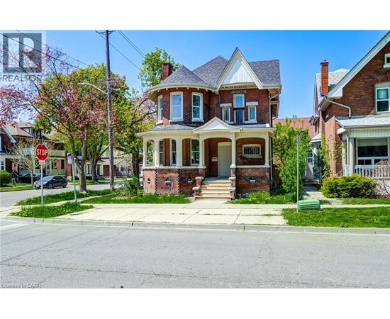 A brick house with a porch and a tree with pink flowers in front.