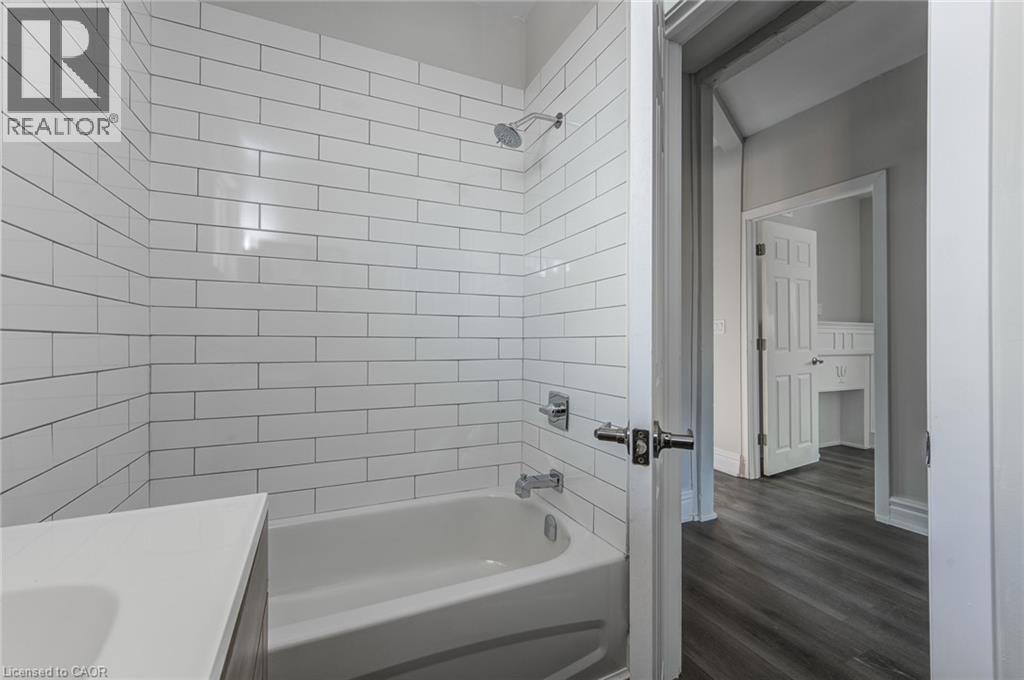 A white tiled bathroom with a bathtub and a doorway leading to a bedroom.