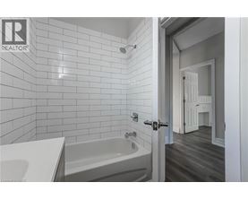 A white tiled bathroom with a bathtub and a doorway leading to a bedroom.