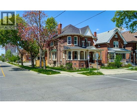 A large red brick house with a porch and a tree in front.
