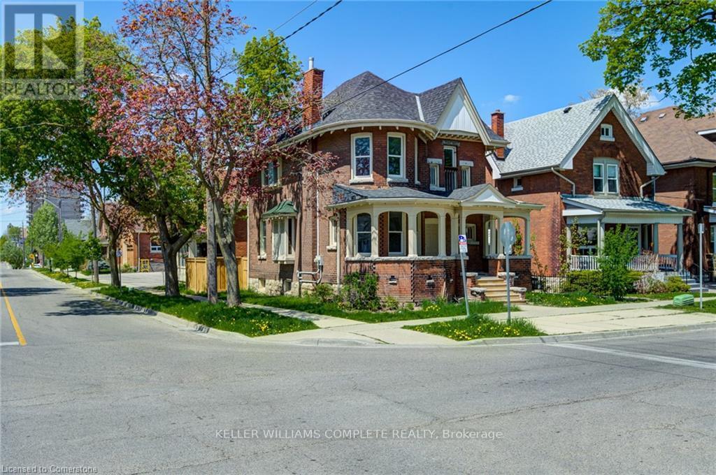 A large brick house with a porch and a tree in front.