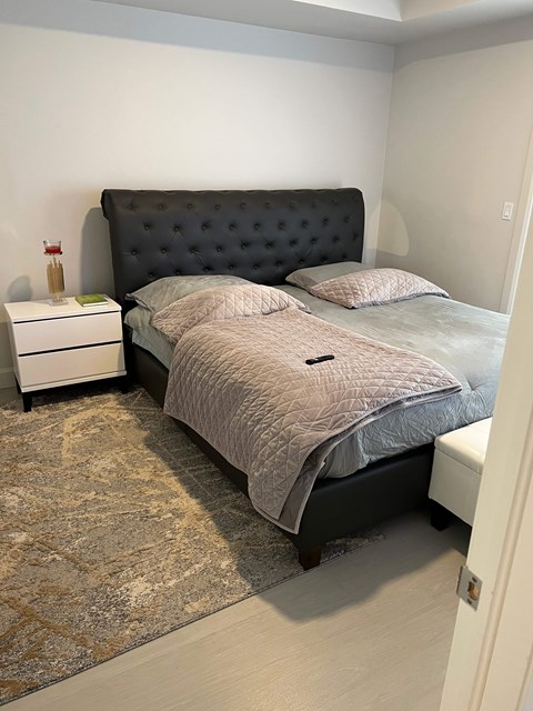 A bedroom with a black tufted headboard bed, a white nightstand, and a patterned rug.