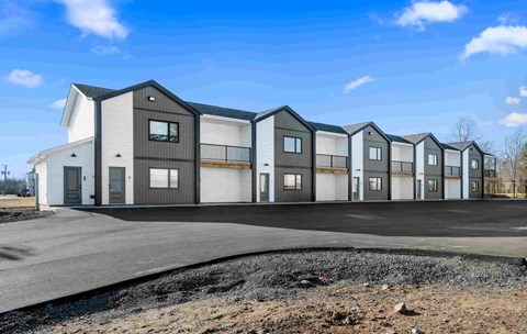 A row of modern townhouses with a gravel driveway in front.