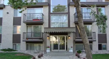A modern apartment building with a balcony and a tree in front.