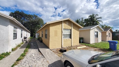 A silver car is parked in front of a yellow house.
