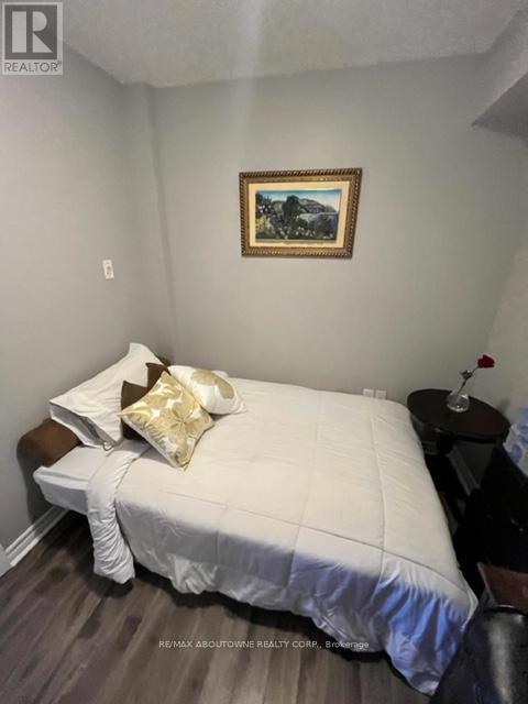 A bedroom with a bed, a small table with a flower vase, and a painting on the wall.