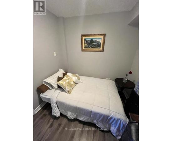 A bedroom with a bed, a small table with a flower vase, and a painting on the wall.