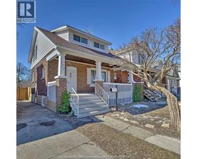 A house with a white porch and a brown roof is for sale.