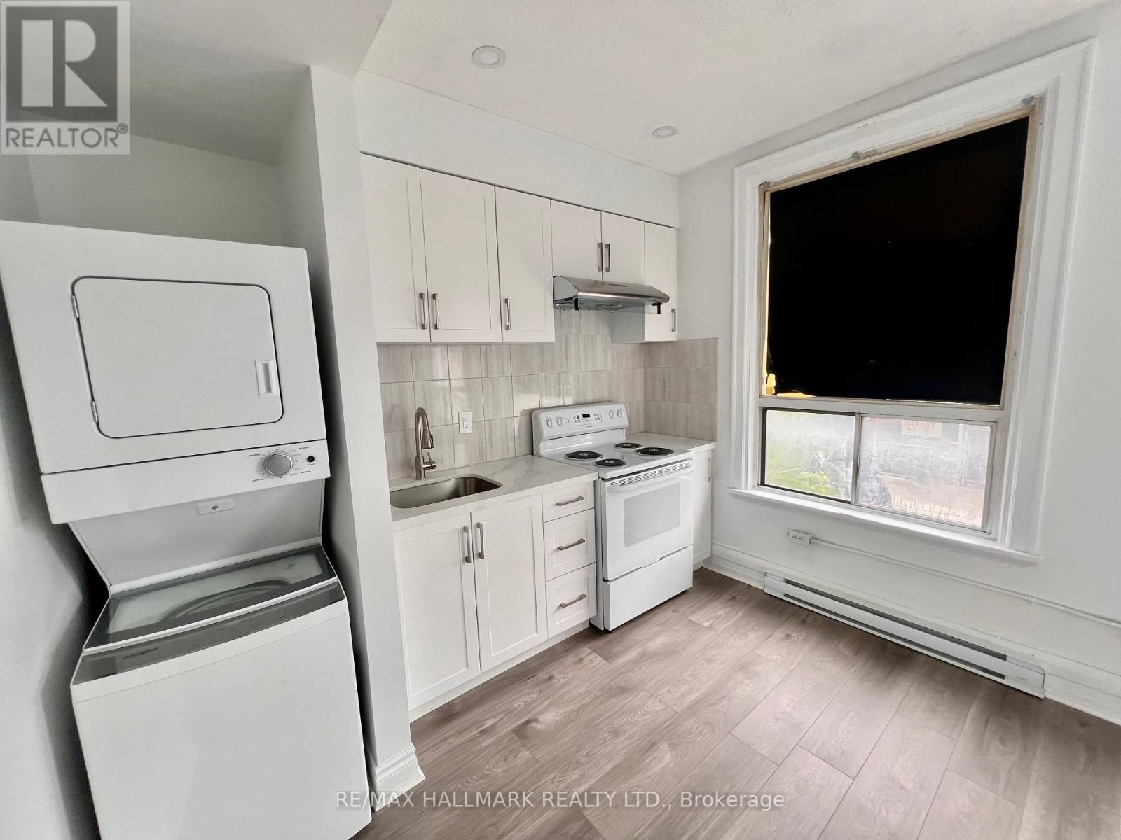 A white washing machine is in a small kitchen with white cabinets.