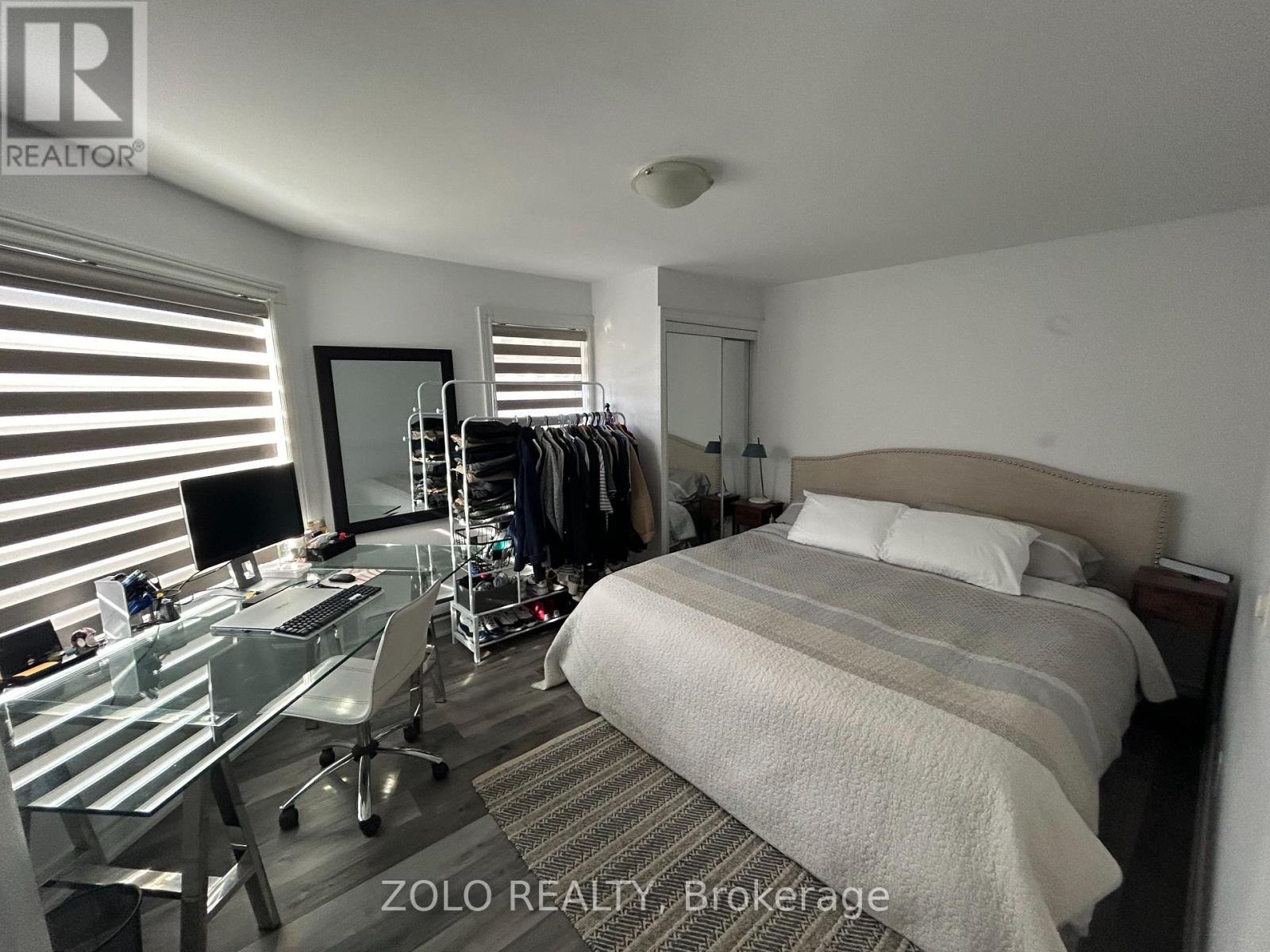 A bedroom with a bed, desk, and clothing rack.