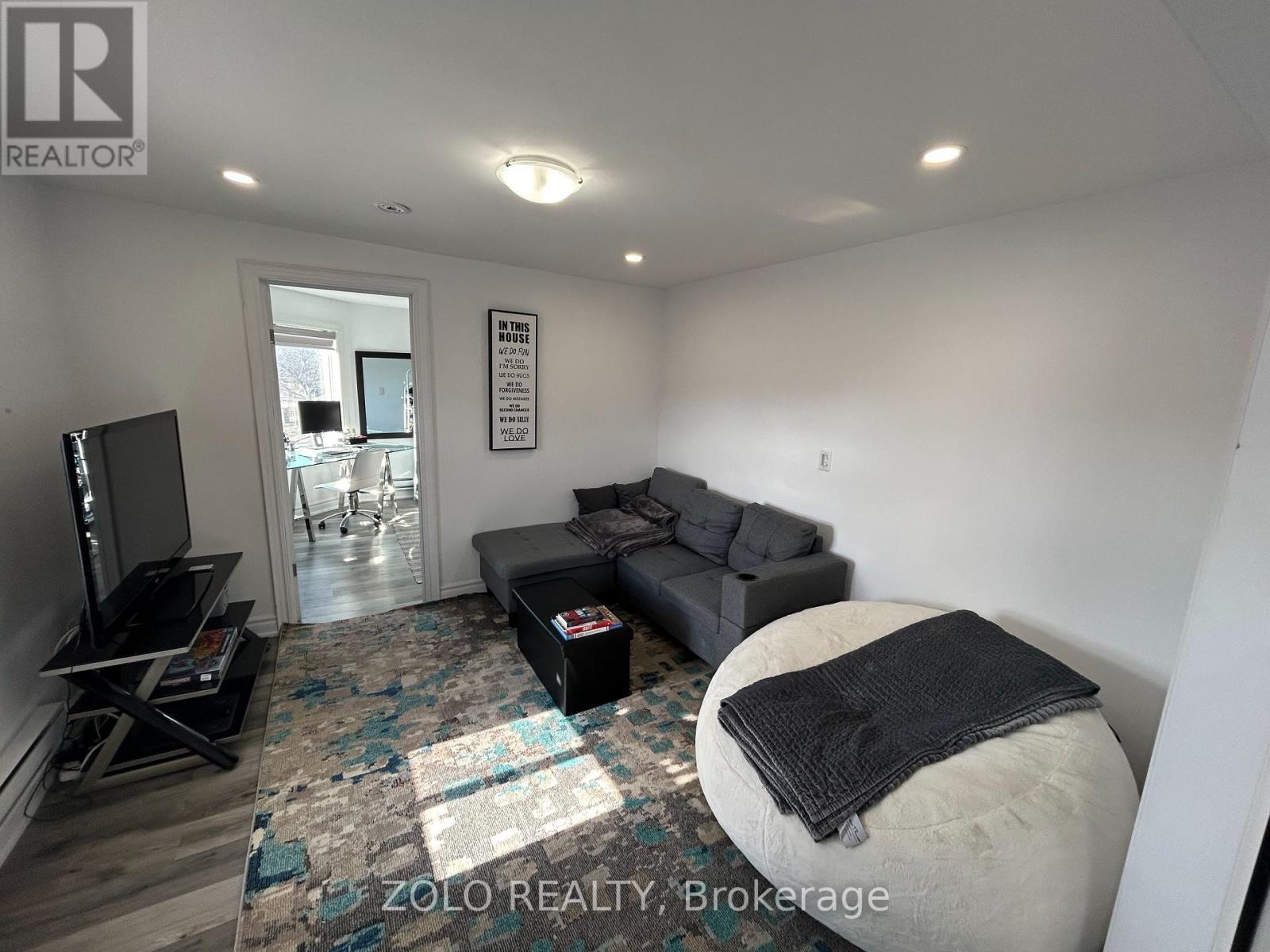 A living room with a grey couch and a black blanket on a white ottoman.