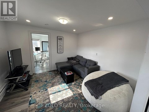 A living room with a grey couch and a black blanket on a white ottoman.
