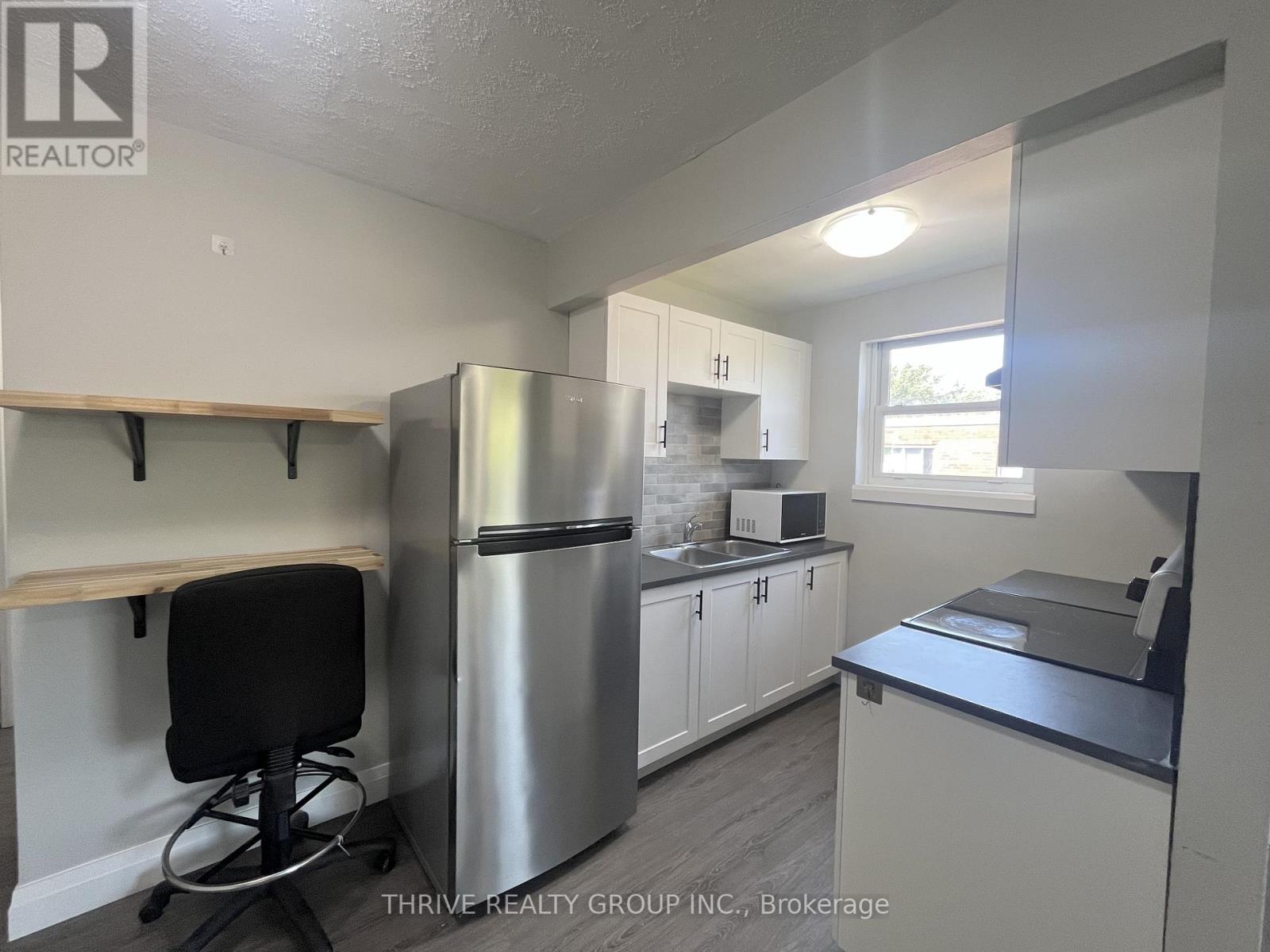 A kitchen with a stainless steel refrigerator, white cabinets, and a black chair.