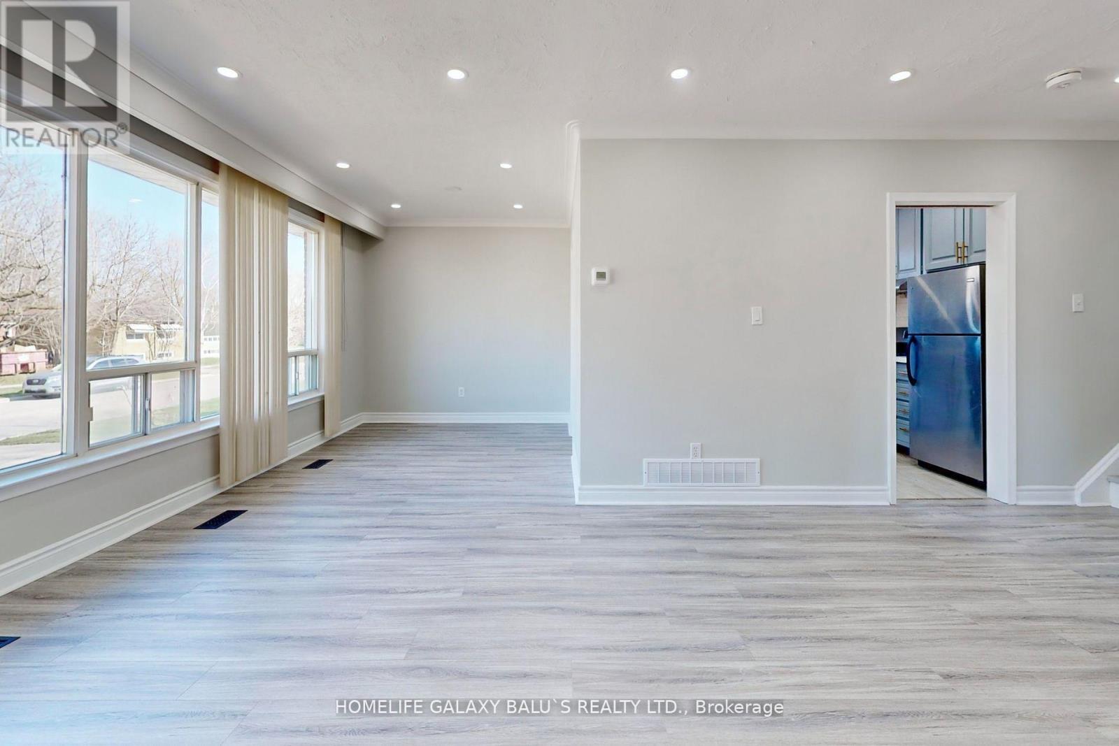 A spacious room with wooden flooring and large windows.