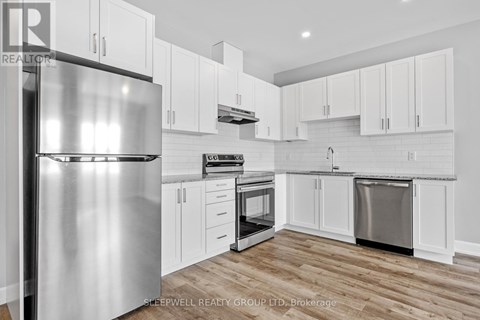 A modern kitchen with a stainless steel refrigerator and wooden flooring.