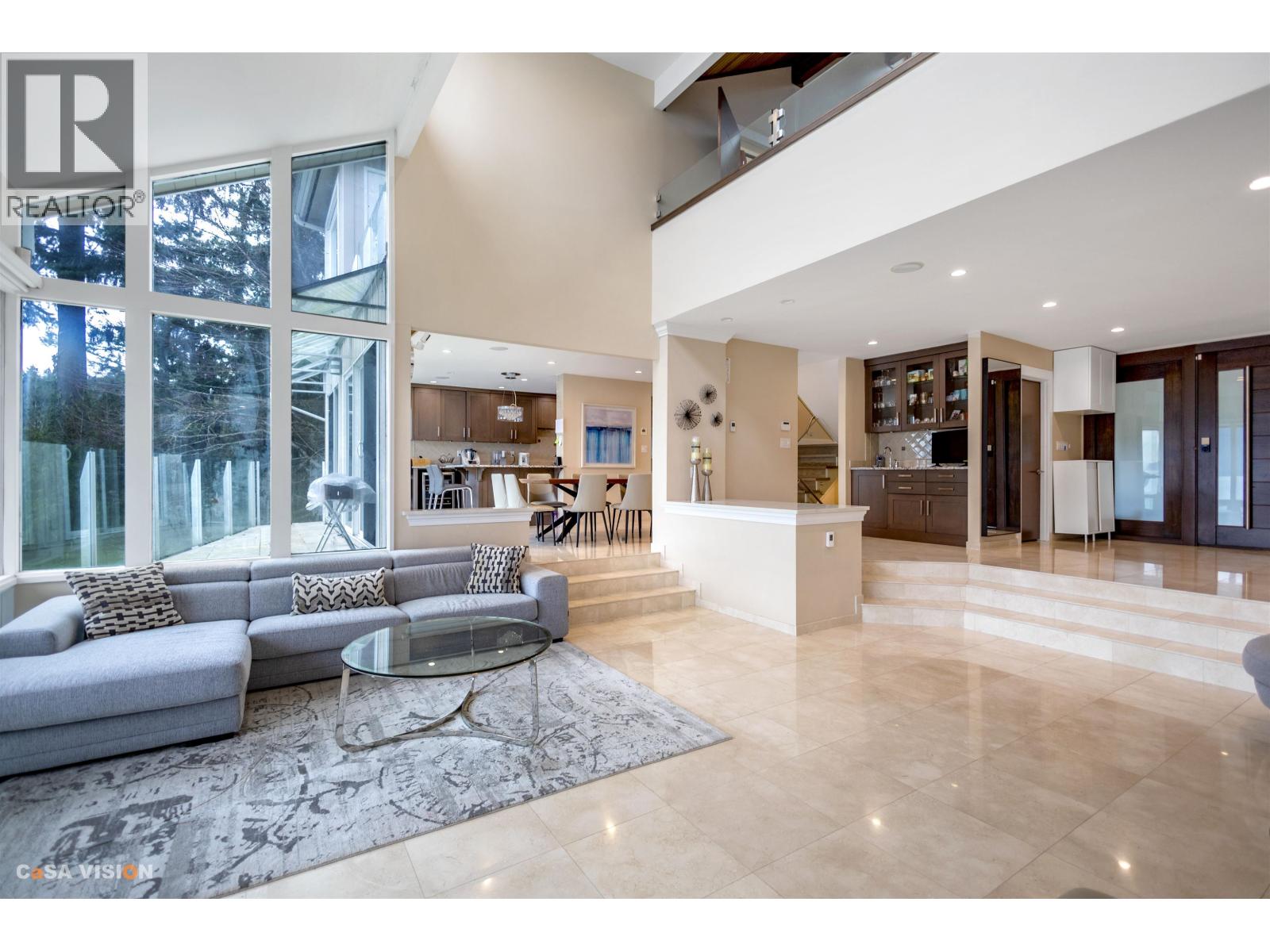 A spacious living room with a grey sofa and a glass coffee table.