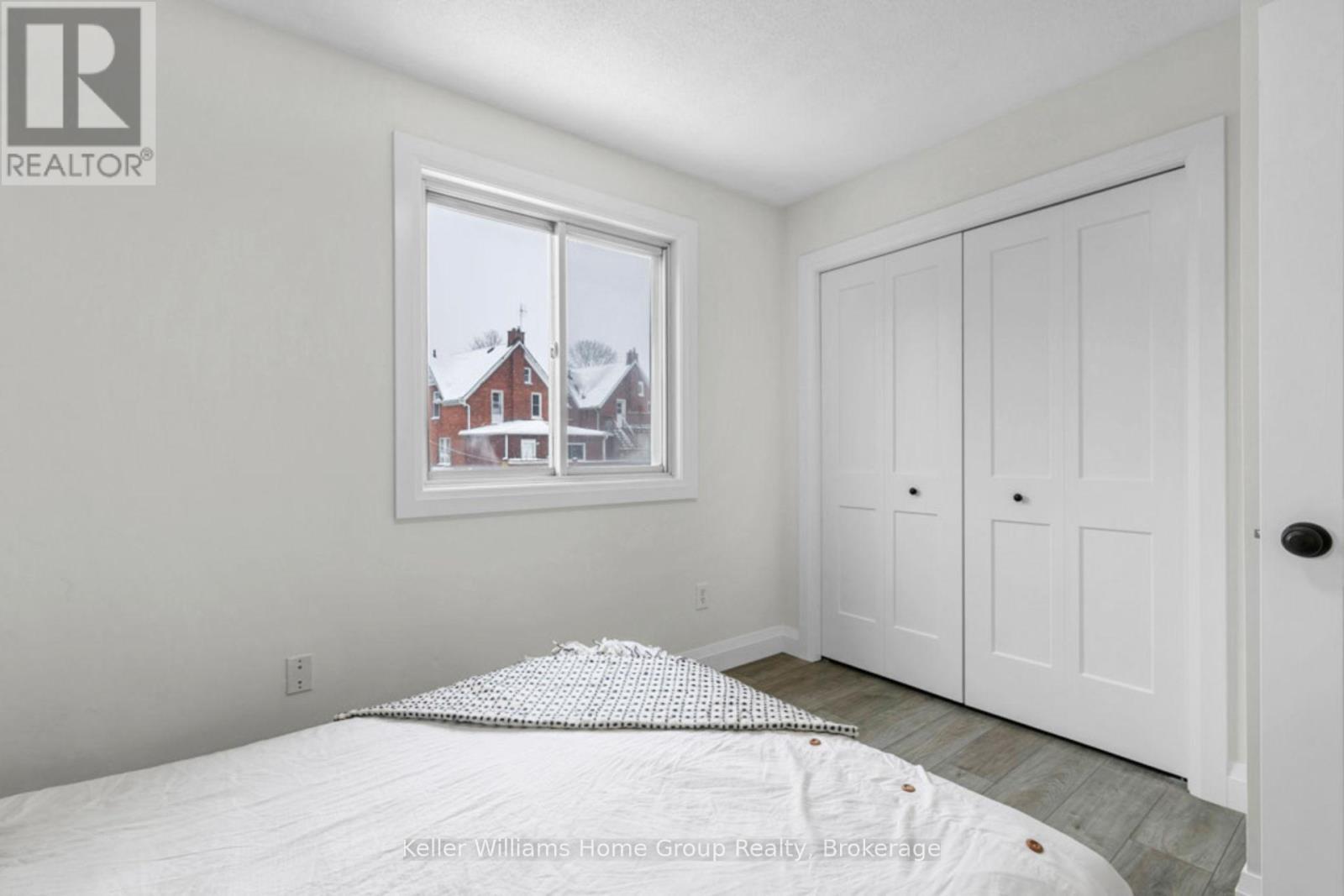 A bedroom with a large bed and a window overlooking a red house.