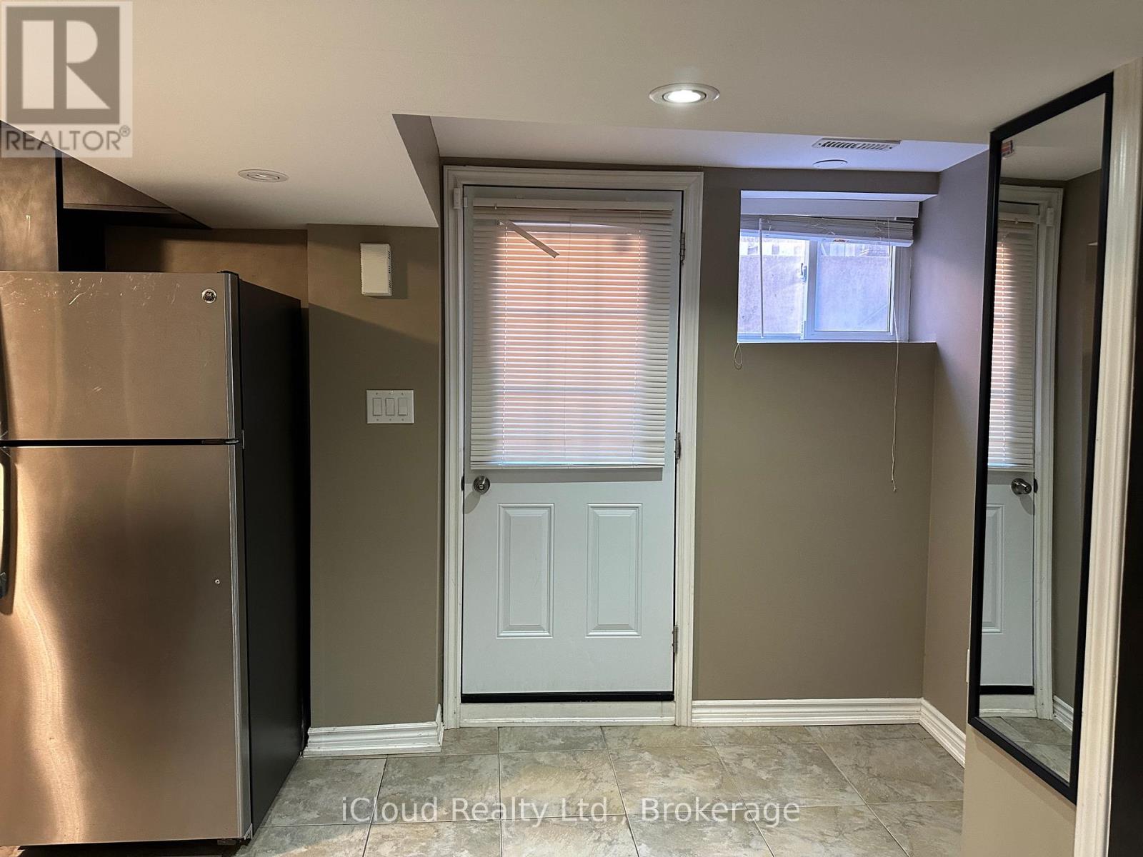 A kitchen with a refrigerator, a door, and a window with blinds.